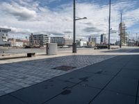 there is a bench on this sidewalk by the water next to buildings and boats in the background