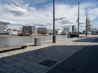 there is a bench on this sidewalk by the water next to buildings and boats in the background