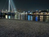 a bench by the water in the city at night time, with buildings reflecting in the water