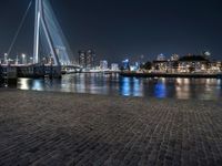 a bench by the water in the city at night time, with buildings reflecting in the water