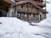 there is a bunch of snow piled on the ground outside of a house in the mountains