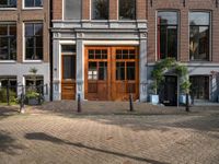 the brick road in front of a brick building has potted plants on it near wooden doors