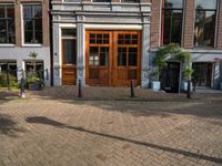 the brick road in front of a brick building has potted plants on it near wooden doors