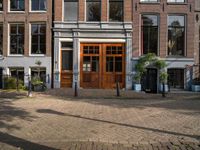 the brick road in front of a brick building has potted plants on it near wooden doors