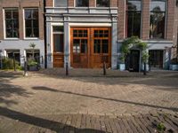 the brick road in front of a brick building has potted plants on it near wooden doors