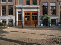 the brick road in front of a brick building has potted plants on it near wooden doors