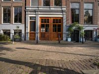 the brick road in front of a brick building has potted plants on it near wooden doors