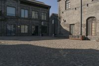 the person is walking down the street near old buildings on a sunny day with a red umbrella