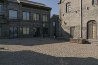 the person is walking down the street near old buildings on a sunny day with a red umbrella