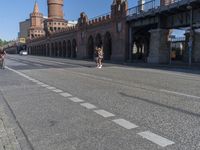 a person walking down a road next to a building and a bridge on a sunny day