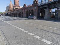 a person walking down a road next to a building and a bridge on a sunny day