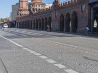 a person walking down a road next to a building and a bridge on a sunny day