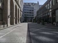 the empty sidewalk with two chairs next to the building on the right side is surrounded by tall windows