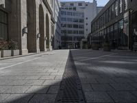 the empty sidewalk with two chairs next to the building on the right side is surrounded by tall windows