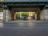 the car is driving beneath the bridge on a street lined with tall buildings and some people