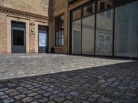 the sidewalk is paved with stones and has a bench in front of it, with no people inside