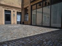 the sidewalk is paved with stones and has a bench in front of it, with no people inside