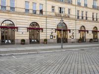 people walking on sidewalk in front of an old hotel building with large windows and doors