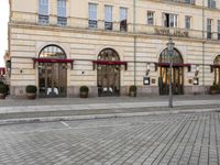 people walking on sidewalk in front of an old hotel building with large windows and doors