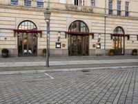 people walking on sidewalk in front of an old hotel building with large windows and doors