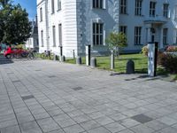 a sidewalk with a sidewalk marker, plants, and a bike in front of a building