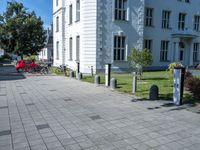 a sidewalk with a sidewalk marker, plants, and a bike in front of a building