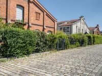 brick path with green bushes on the side and large brick building in back ground at center