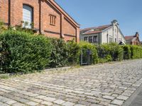 brick path with green bushes on the side and large brick building in back ground at center