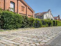 brick path with green bushes on the side and large brick building in back ground at center