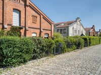 brick path with green bushes on the side and large brick building in back ground at center