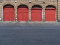 three fire hydrants in front of red doors on a brick building in an urban area