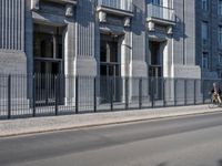 an individual is riding a bicycle on the street next to a building with columns and windows