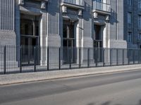 an individual is riding a bicycle on the street next to a building with columns and windows