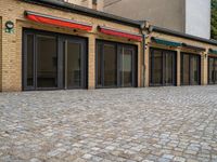 the bricked building with black doors has three red and green awnings over them