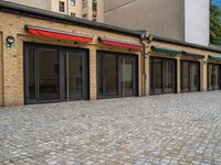 the bricked building with black doors has three red and green awnings over them