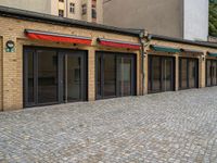 the bricked building with black doors has three red and green awnings over them