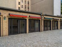 the bricked building with black doors has three red and green awnings over them