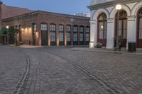 brick paved square outside a large building with double doors in the center and plants on either side of the door