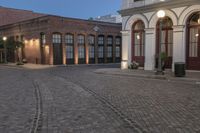 brick paved square outside a large building with double doors in the center and plants on either side of the door