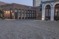 brick paved square outside a large building with double doors in the center and plants on either side of the door