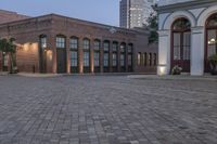 brick paved square outside a large building with double doors in the center and plants on either side of the door