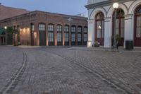 brick paved square outside a large building with double doors in the center and plants on either side of the door