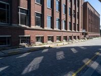 a narrow brick road leads to a tall brick building with many windows on each side of it