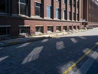 a narrow brick road leads to a tall brick building with many windows on each side of it