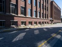 a narrow brick road leads to a tall brick building with many windows on each side of it