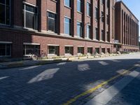 a narrow brick road leads to a tall brick building with many windows on each side of it