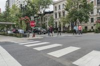 several people walking across the street by an intersection and stop sign in a city setting