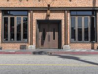 a parking meter is in front of a building with large windows and a brick wall