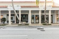 a white and tan building sitting next to a parking space with a palm tree in front of it