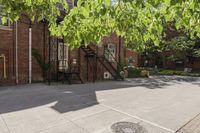 an old brick building with a staircase and sidewalk on both sides of a street with plants growing on the sidewalk